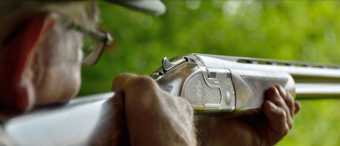 Closeup of shotgun while a gentleman aims at a clay while shooting at Lady's Wood Shooting School